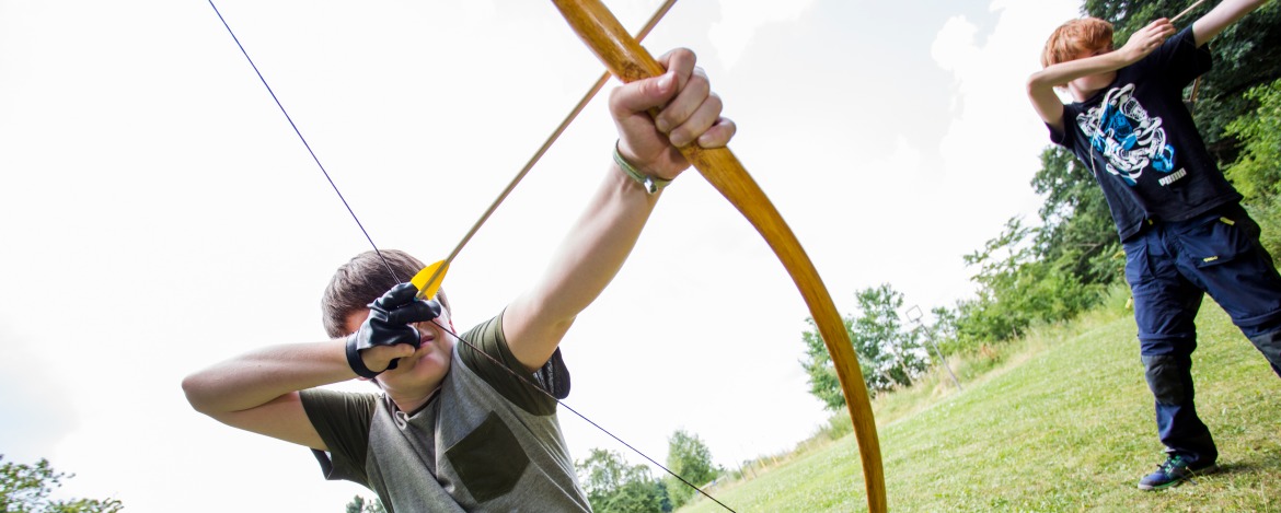 Zwei Personen beim Bogenschießen, die im Freien die Bögen spannen und zielen.